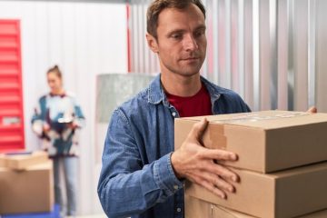 A man carries a stack of boxes in a self-storage room, organizing his belongings efficiently.