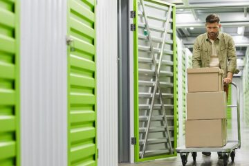 A man pushes a cart filled with boxes in a self-storage room, organizing his belongings efficiently.