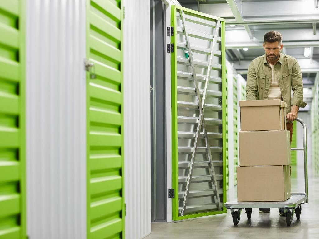 A man pushes a cart filled with boxes in a self-storage room, organizing his belongings efficiently.