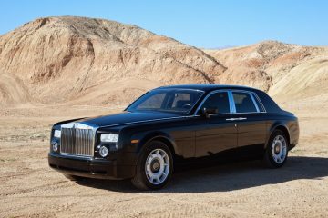 A sleek black Rolls Royce parked in a vast desert, showcasing luxury amidst the arid landscape. Seasonal car storage option available.