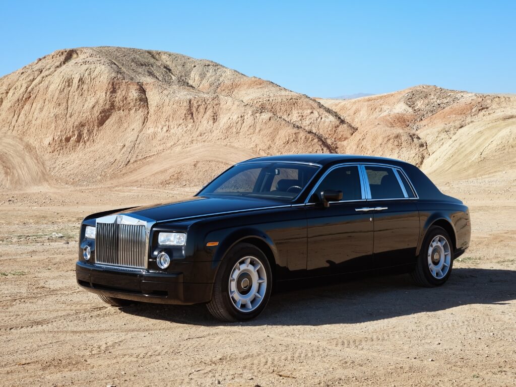 A sleek black Rolls Royce parked in a vast desert, showcasing luxury amidst the arid landscape. Seasonal car storage option available.